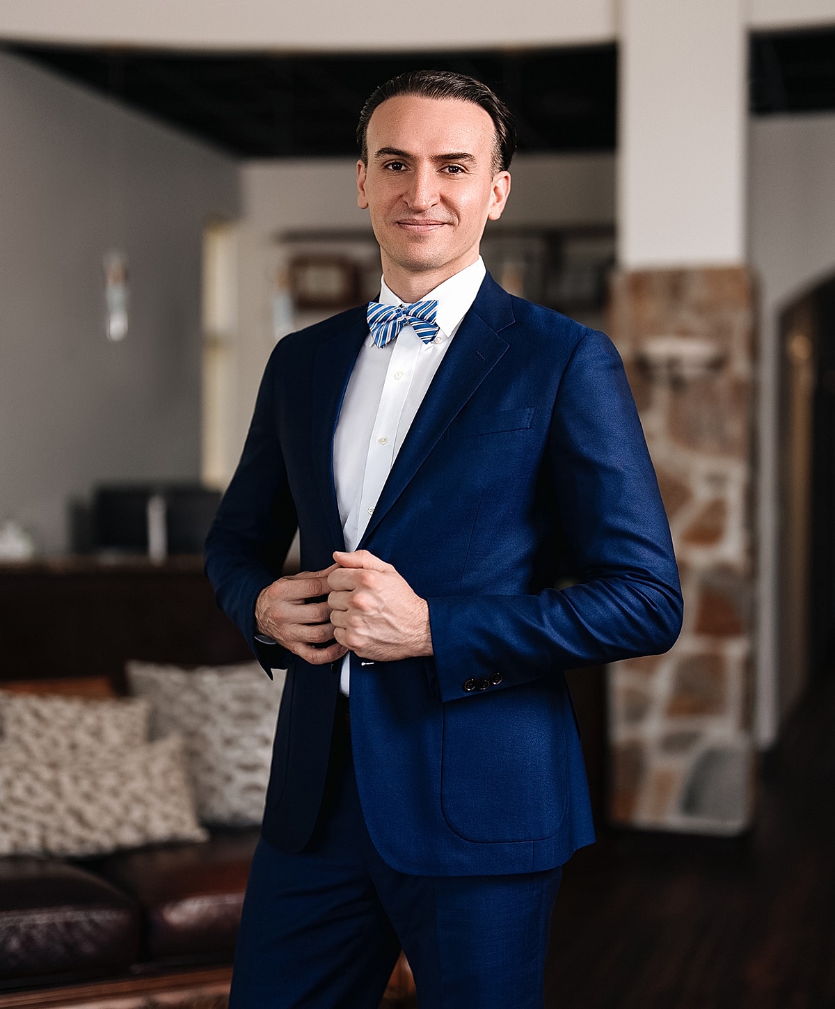 Man in navy suit and bowtie, smiling confidently.