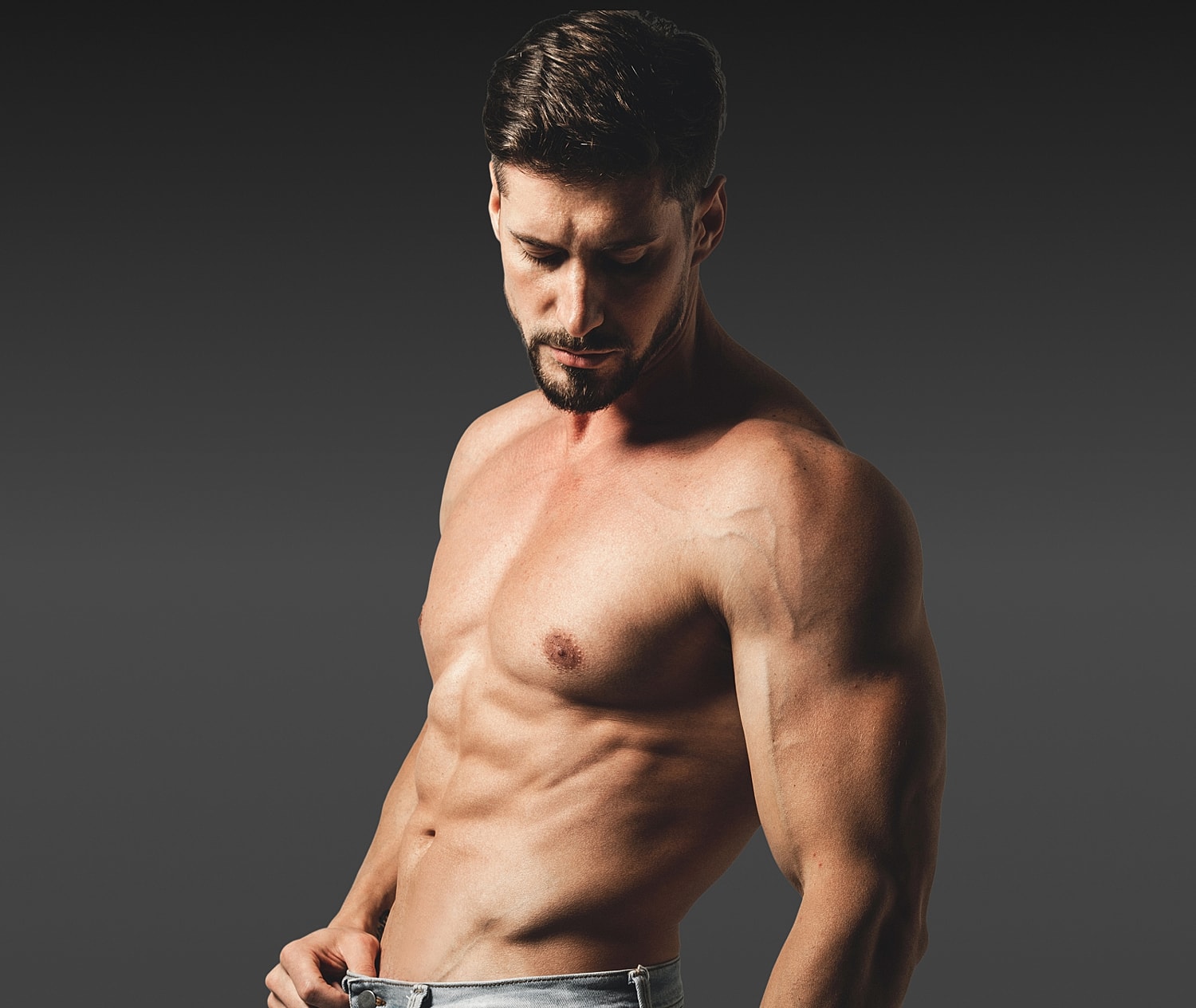 Muscular Houston plastic surgery model posing against a dark background.